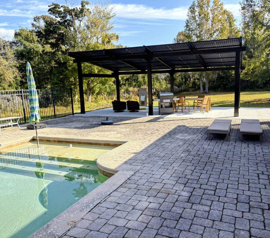 Solar pergola creating a shaded outdoor living and dining space beside a pool
